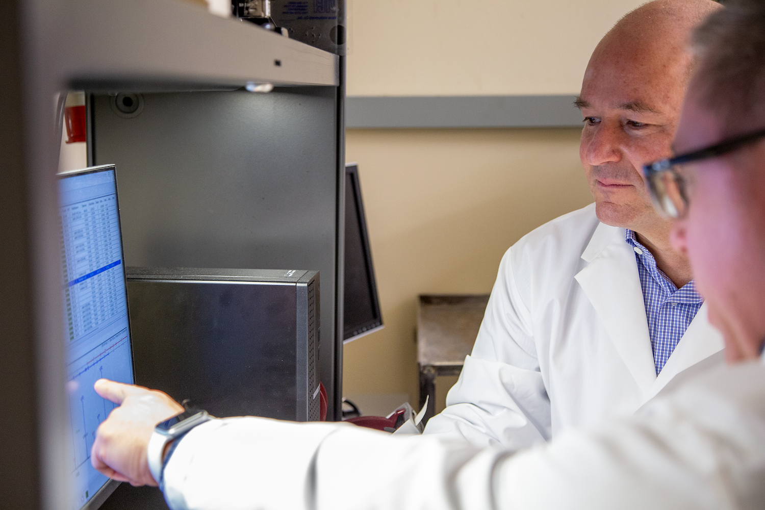 Researchers in lab coats review proteomics data displayed on a computer monitor.