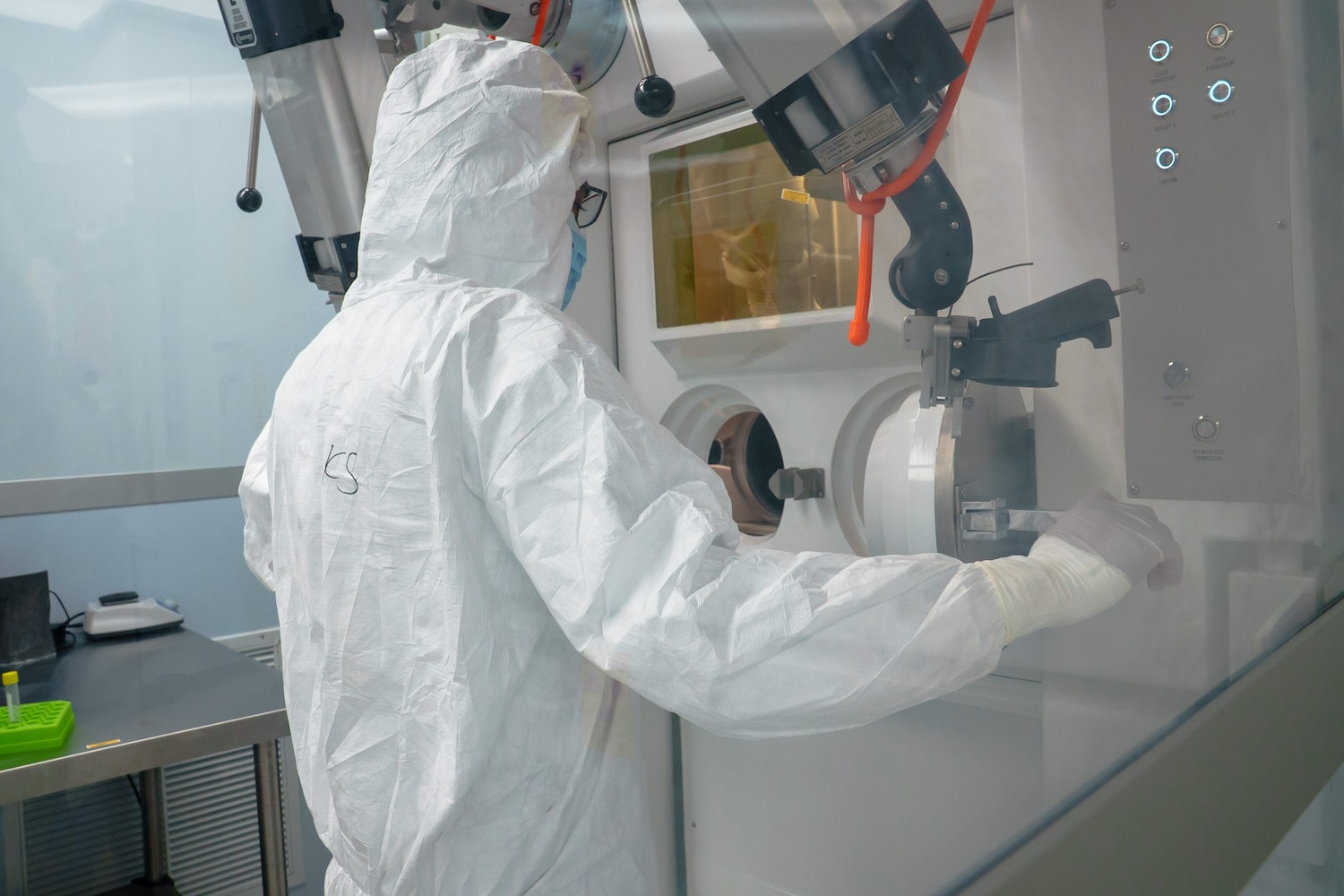 A researcher in full protective cleanroom gear operates specialized radiation research equipment inside a controlled laboratory space.